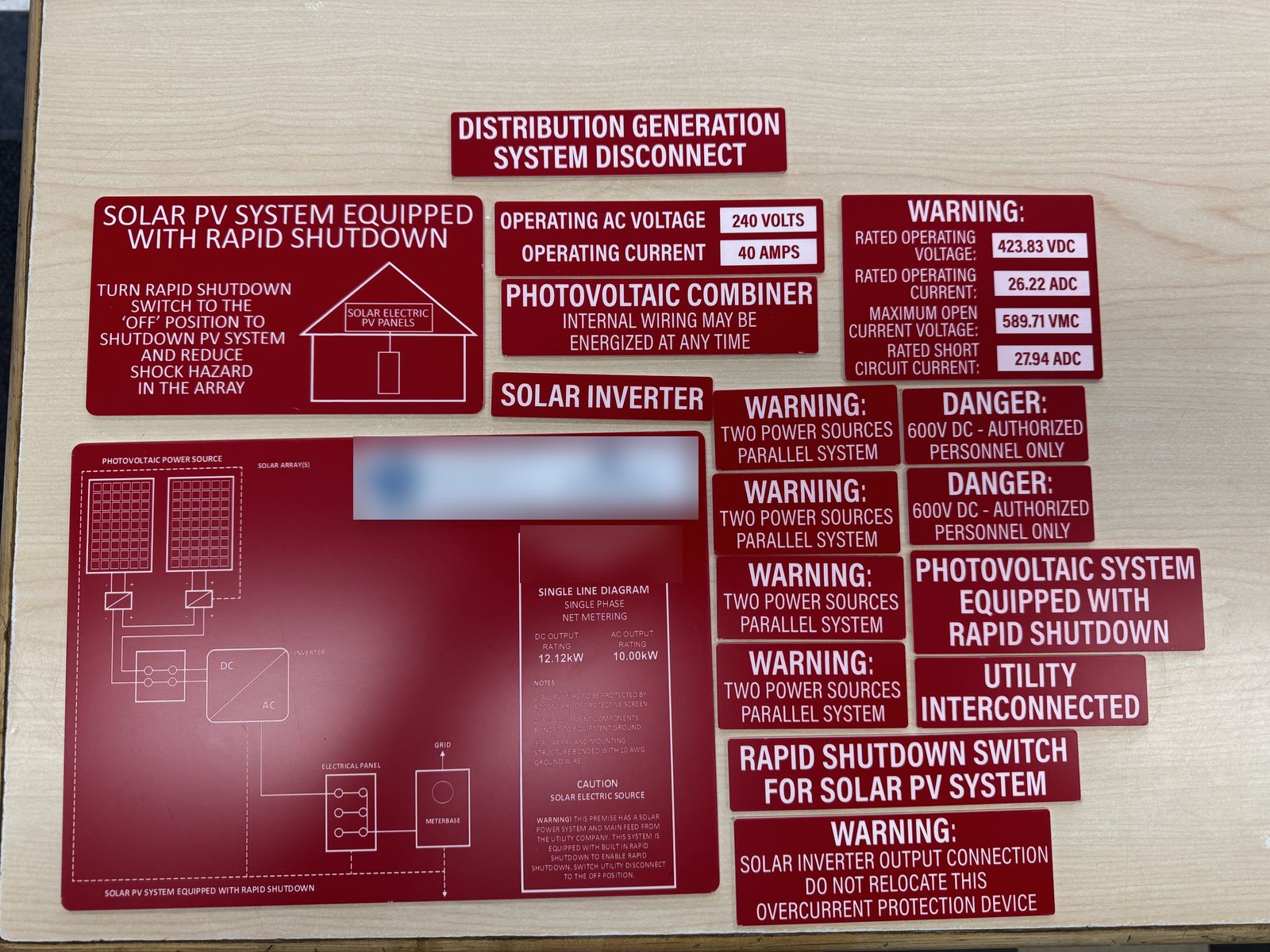 Set of white-on-red lamacoid solar labels and a single-line diagram plate laid out on a table